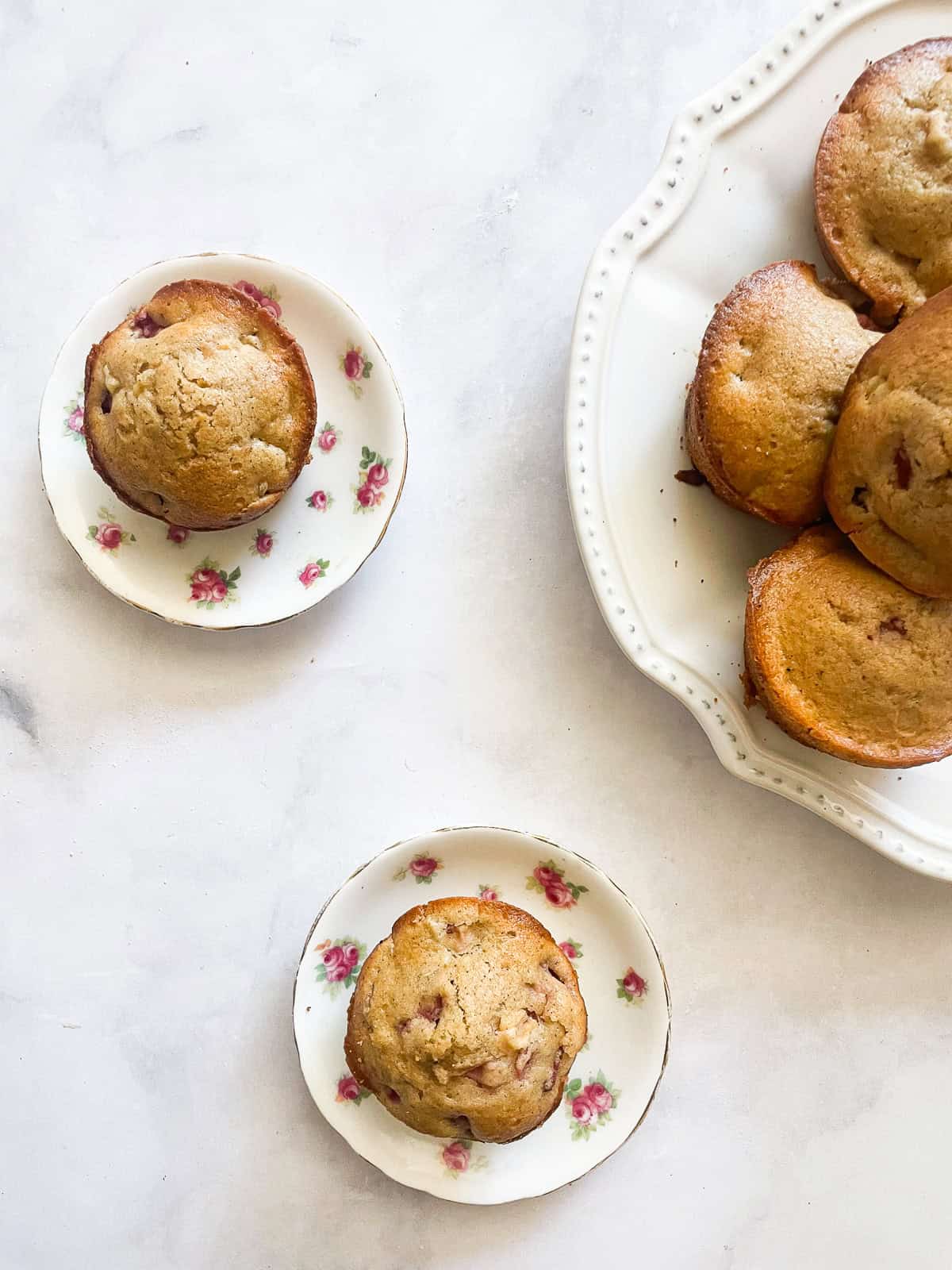 These gluten free strawberry muffins are made with fresh strawberries and tangy buttermilk for a tender, fruit-filled breakfast bite. Two gluten free strawberry muffins on flowered plates next to a plate of muffins.