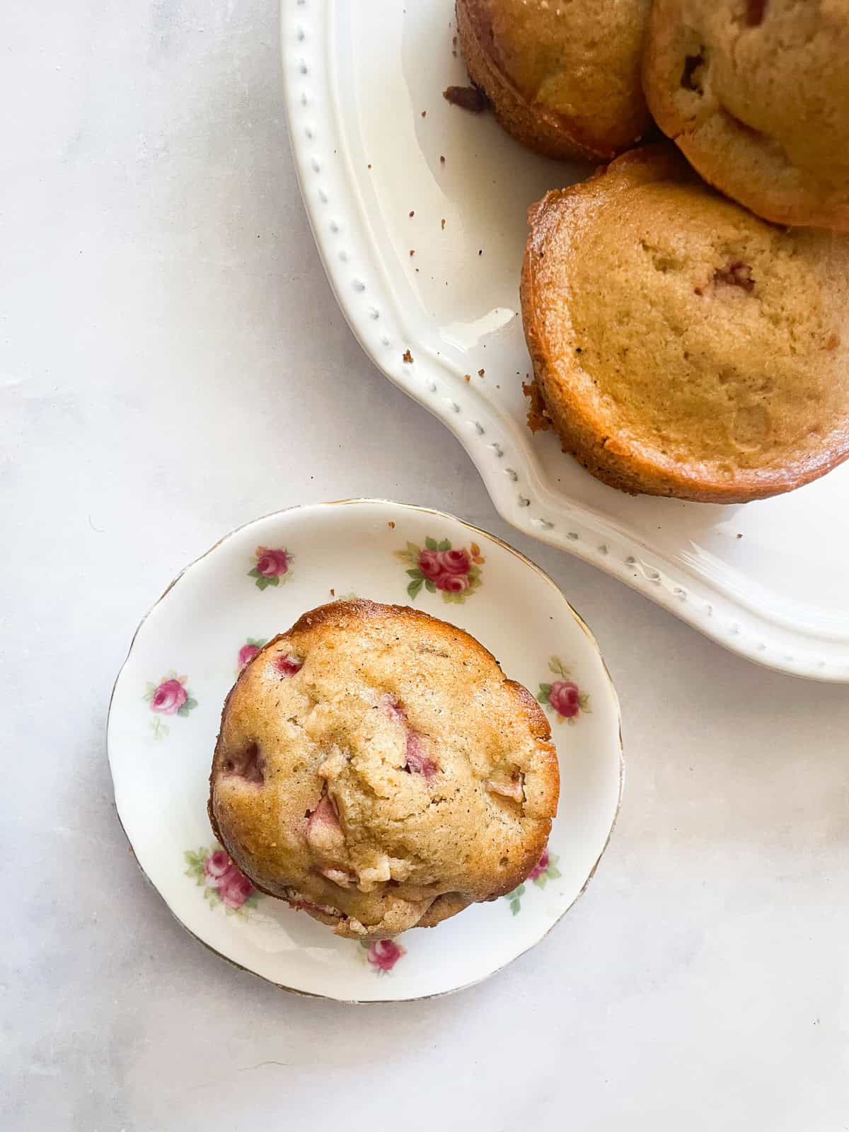 A gluten free strawberry muffin on a plate next to a plate of muffins.