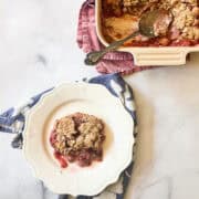 A pan of gluten free strawberry rhubarb crisp with a spoon and a plate of crisp.