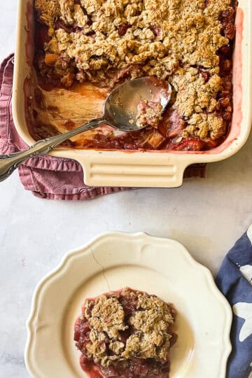 A pan of gluten free strawberry rhubarb crisp with a spoon and a plate of crisp.