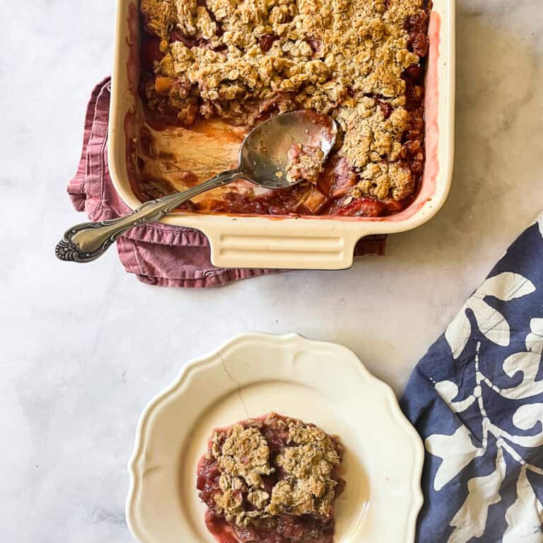 A pan of gluten free strawberry rhubarb crisp with a spoon and a plate of crisp.