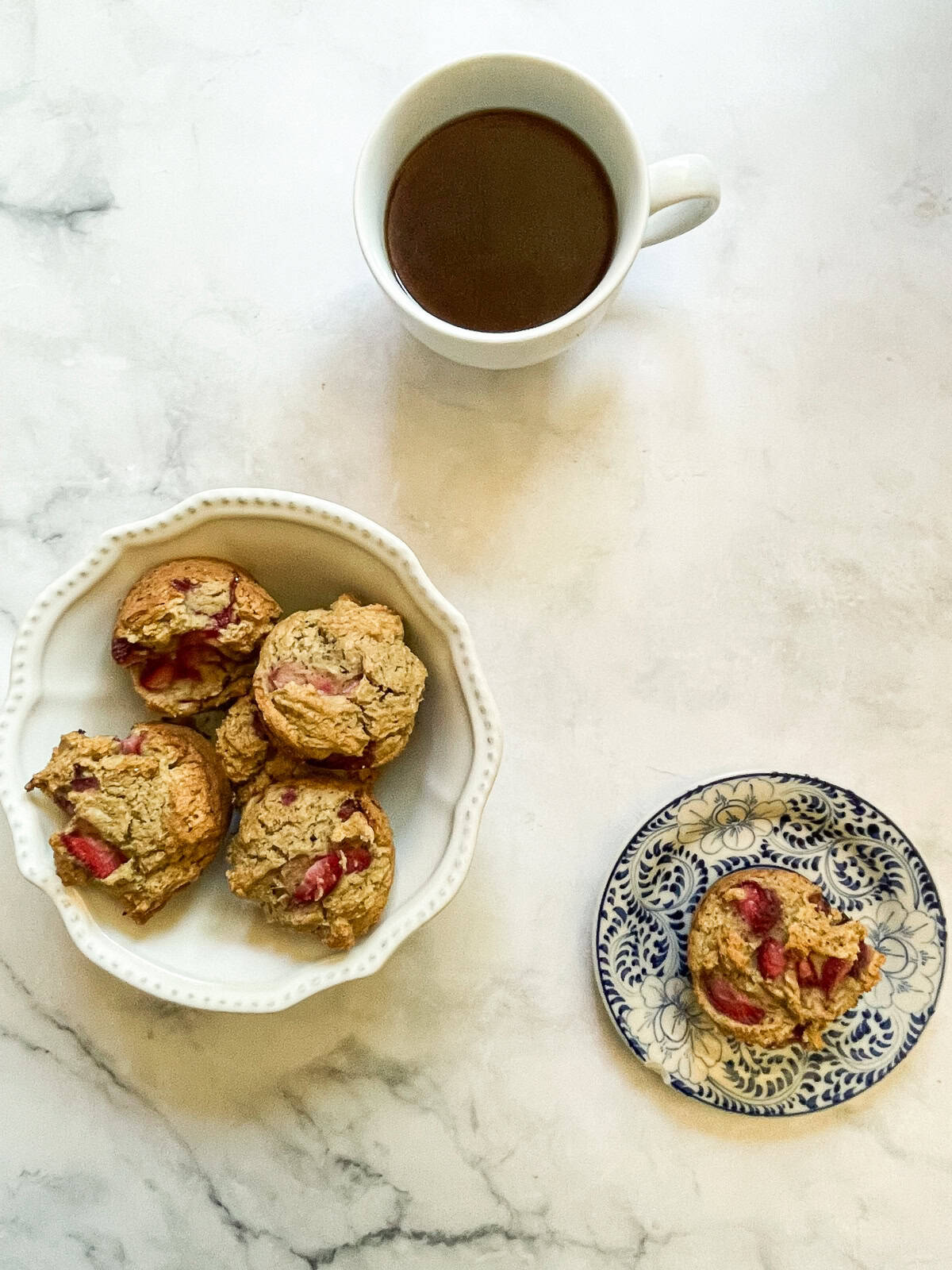 A cup of tea, a bowl of strawberry muffins, and a muffin on a plate.