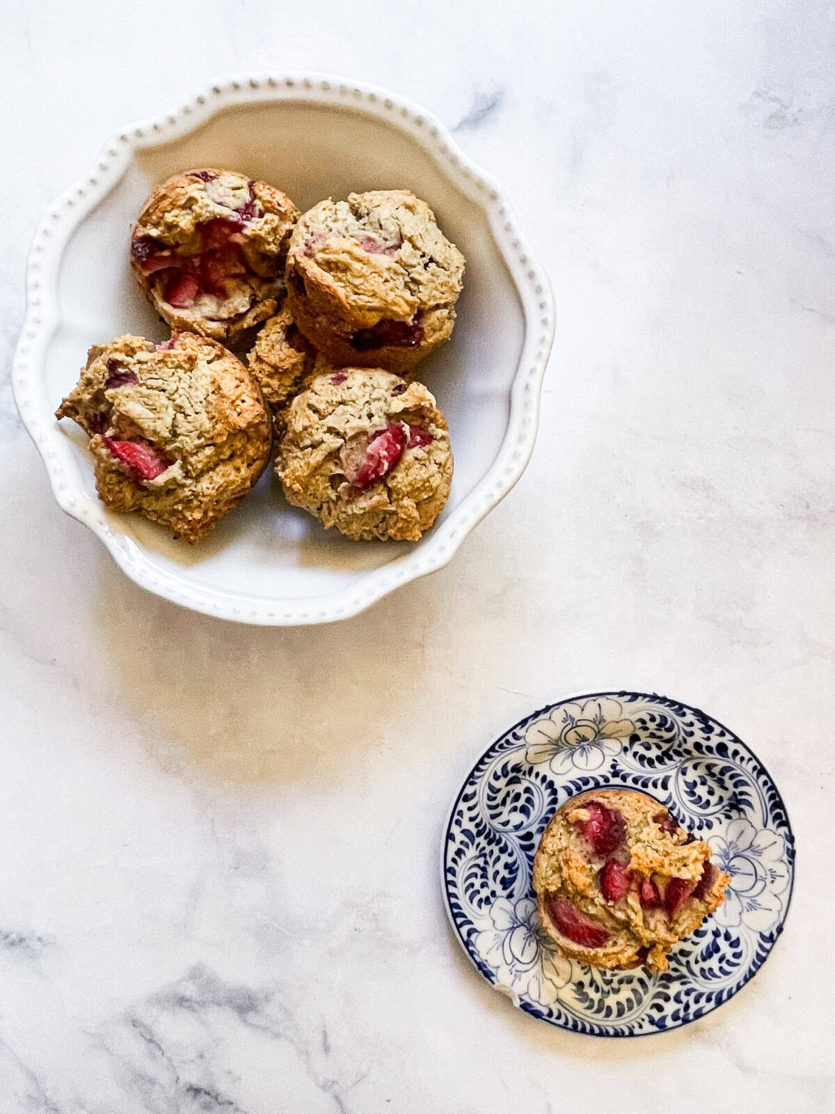 A white bowl of gluten free and vegan strawberry muffins and a muffin on a plate.