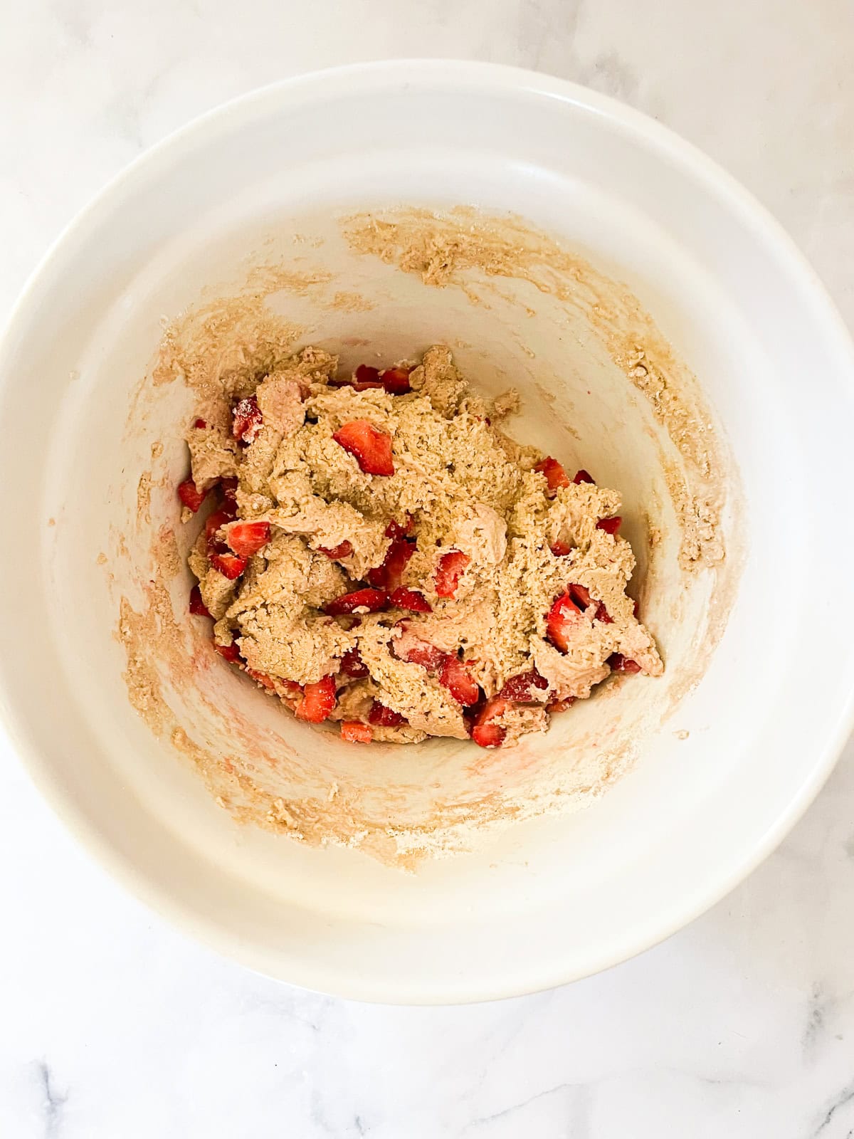 Strawberries are added to a bowl of muffin batter.