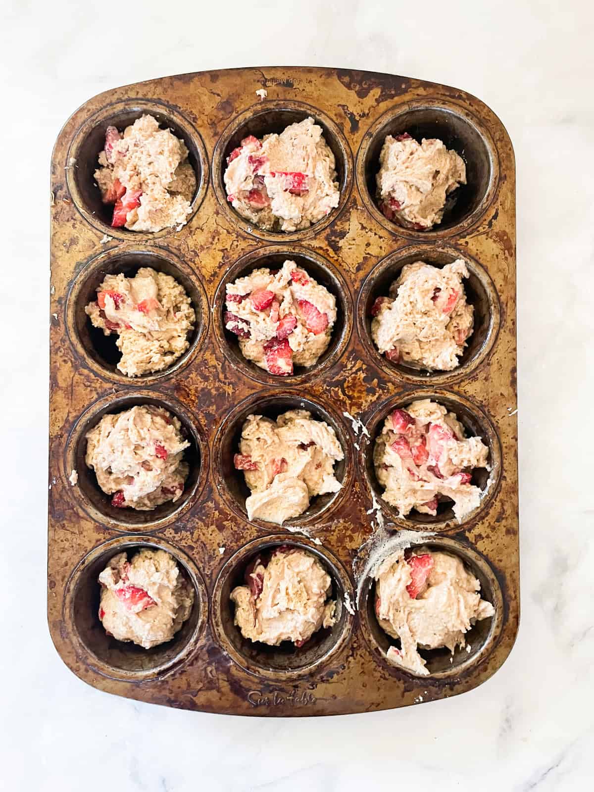 Vegan strawberry muffin batter in a muffin tin.