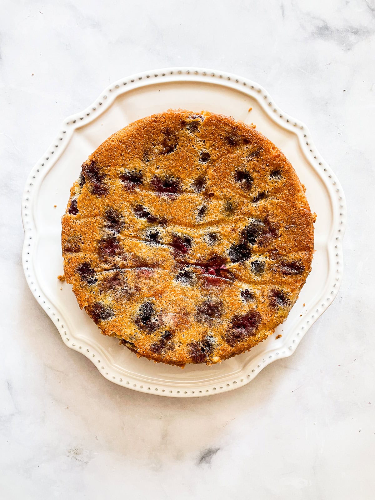 This rustic gluten-free cherry torte tucks sweet, fresh cherries into a tender, buttery cake made with just two simple gluten-free flours. A whole gluten free cherry torte on a white plate.