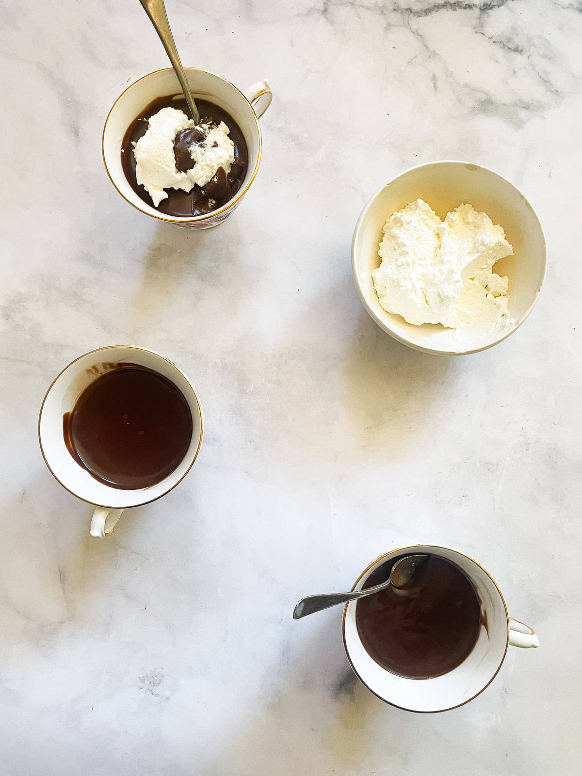 Cups of gluten free chocolate pudding with spoons and a bowl of whipped cream.