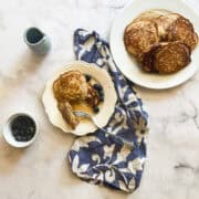 Gluten free oatmeal pancakes surrounded by a jug of maple syrup and blueberries.