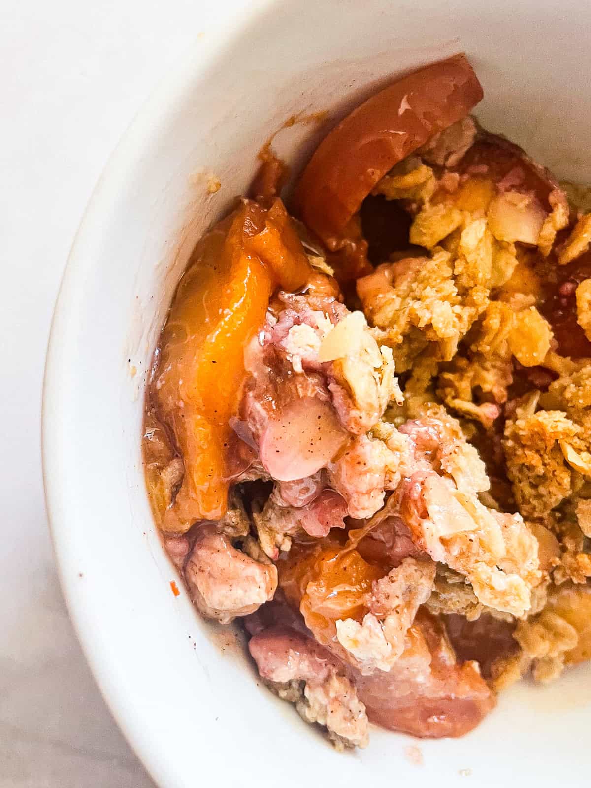 This gluten-free peach crisp stars juicy fresh peaches tucked under a rich toasted oat topping. Must be served with vanilla ice cream! A close up of a bowl of gluten free peach crisp.