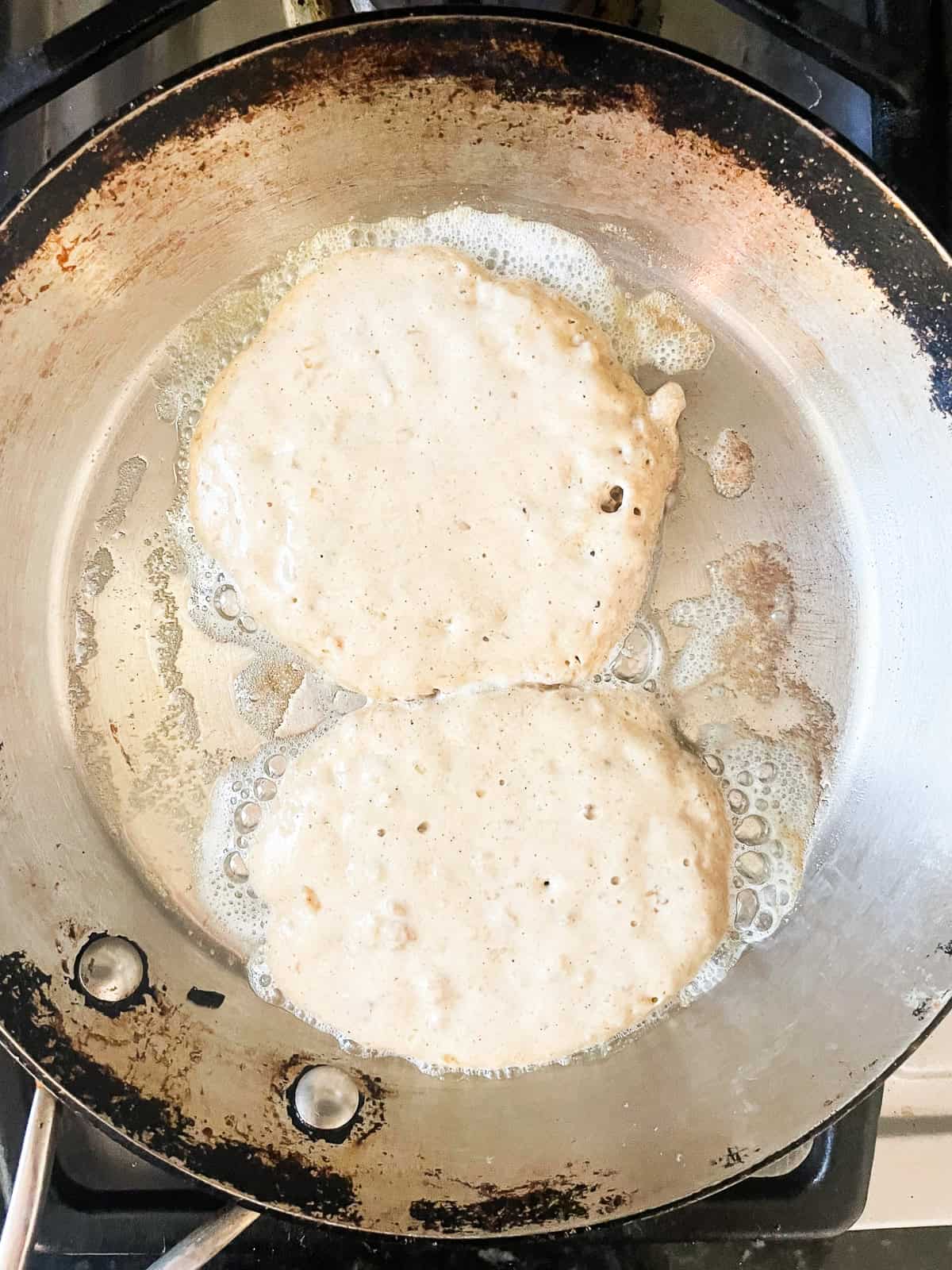 These gluten free oatmeal pancakes are hearty, wholesome, and filling! Made with oat flour, leftover oatmeal, and a touch of maple syrup. Two gluten free oatmeal pancakes cook in a pan.