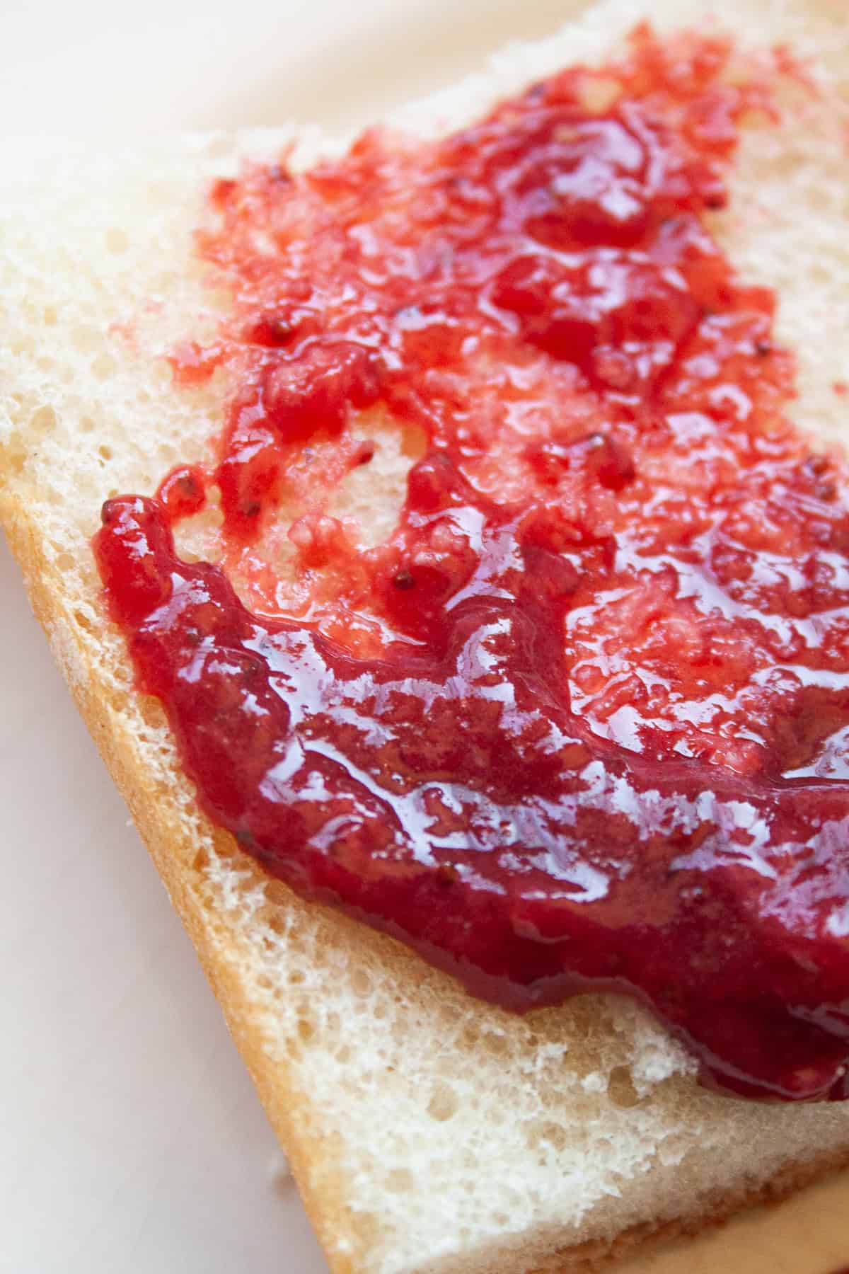 A recipe for a beautifully hued, low sugar strawberry jam that's also made without pectin. You can make this a refrigerator jam or can it. Strawberry jam on a piece of bread.