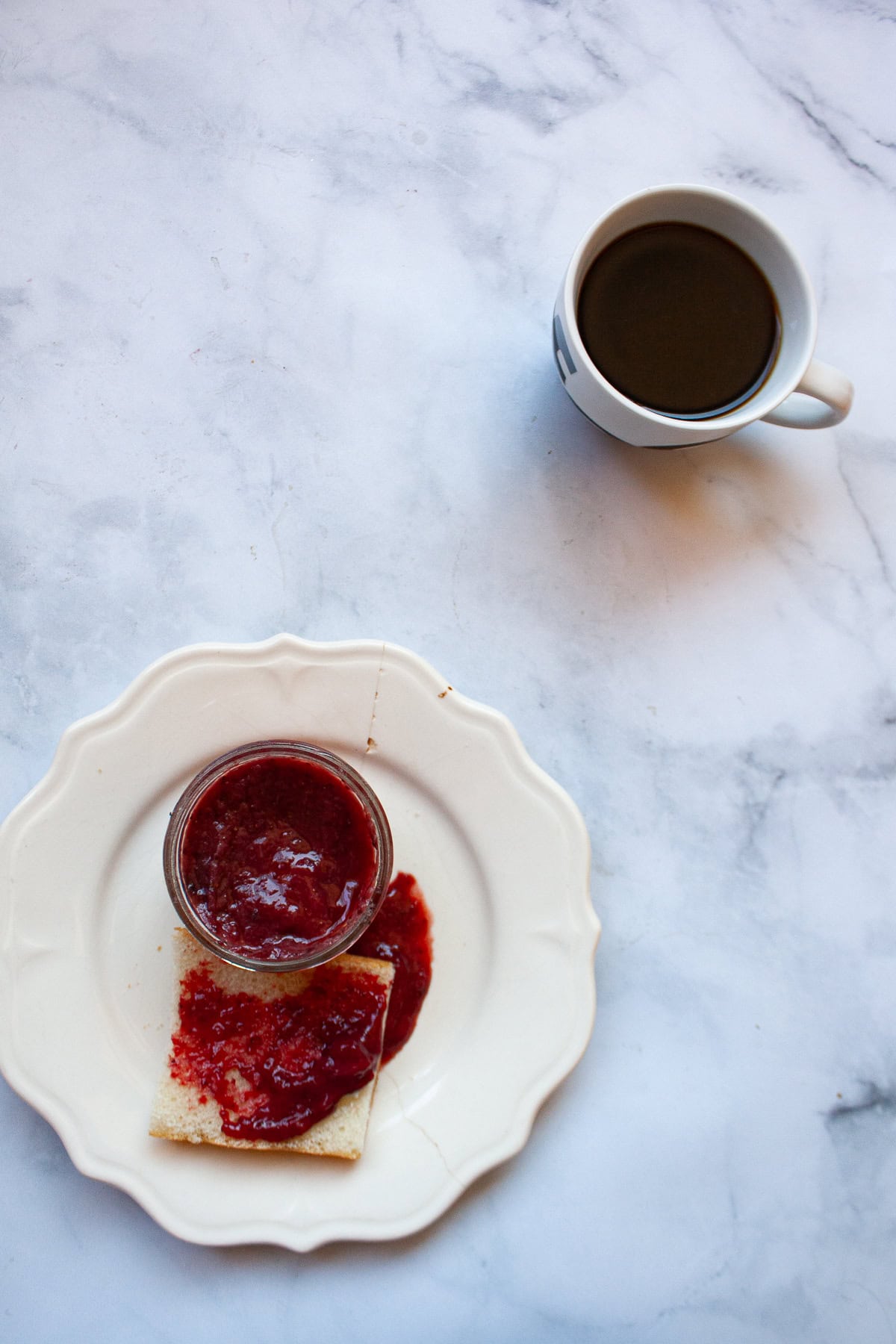 A recipe for a beautifully hued, low sugar strawberry jam that's also made without pectin. You can make this a refrigerator jam or can it. Low sugar strawberry jam on a plate and a cup of coffee next to it.