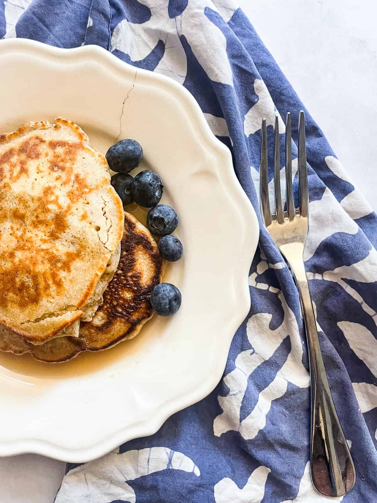 Tender and fluffy oat flour pancakes are made with oat flour for a gorgeous, naturally gluten-free breakfast option. A one-bowl recipe! Blueberries next to a stack of oat flour pancakes.