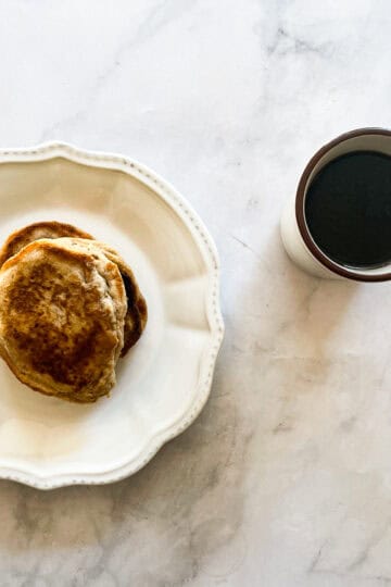 A decorative plate with oat flour pancakes next to a cup of coffee.