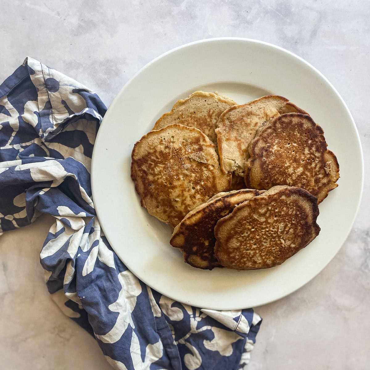A plate of oat flour pancakes next to a blue and white napkin.