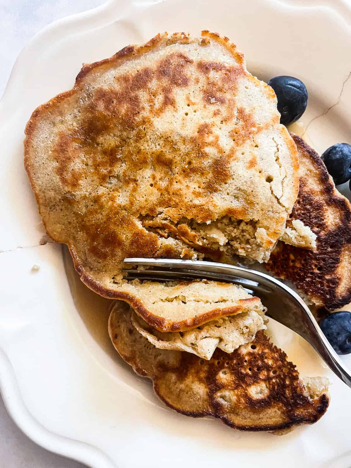 Tender and fluffy oat flour pancakes are made with oat flour for a gorgeous, naturally gluten-free breakfast option. A one-bowl recipe! A fork cuts into a stack of oat flour pancakes.