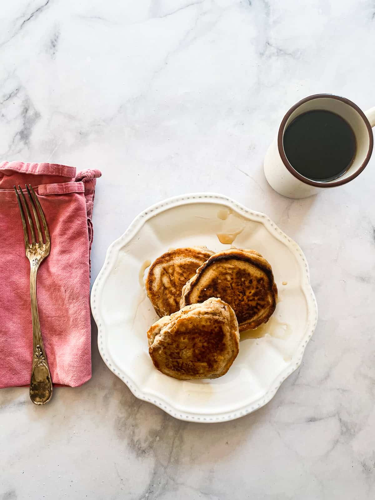 Tender and fluffy oat flour pancakes are made with oat flour for a gorgeous, naturally gluten-free breakfast option. A one-bowl recipe! A plate of oat flour pancakes next to a red napkin, a for, and a cup of cofee.