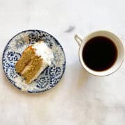 A slice of jammy rhubarb cake with whipped cream and a cup of tea.