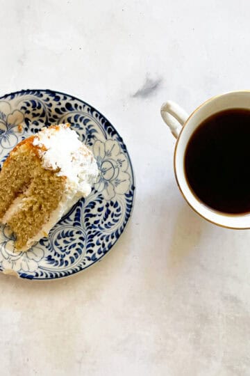 A slice of jammy rhubarb cake with whipped cream and a cup of tea.