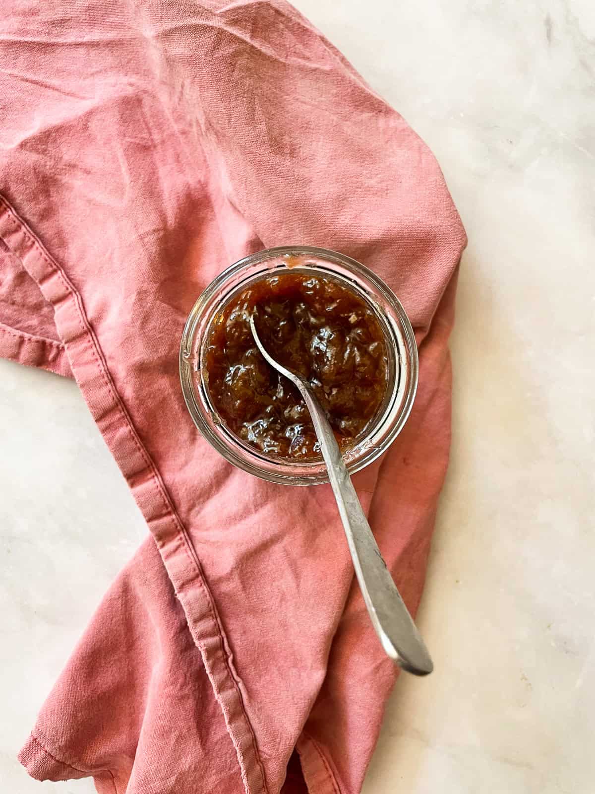 Strawberry & rhubarb jam is probably the loveliest and most fragrant of jams. Bright pink, perfectly sweet-tart, and easy to make. A jar of strawberry and rhubarb jam on a red napkin with a spoon.