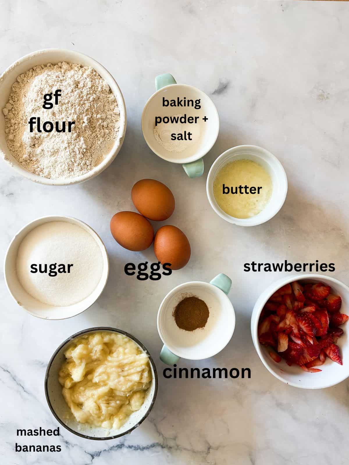 This one-bowl, gluten free easy banana strawberry bread comes together in minutes, and features plenty of chopped fresh strawberries and a kick of cinnamon. Ingredients for easy banana strawberry bread are text-labeled and portioned out.