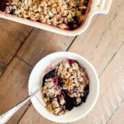 A pan of gluten free apple blackberry crisp next to a bowl of crisp.