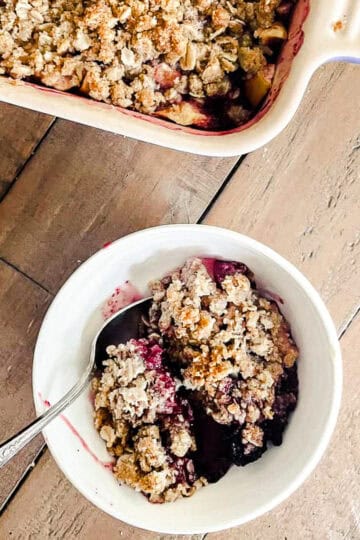 A pan of gluten free apple blackberry crisp next to a bowl of crisp.