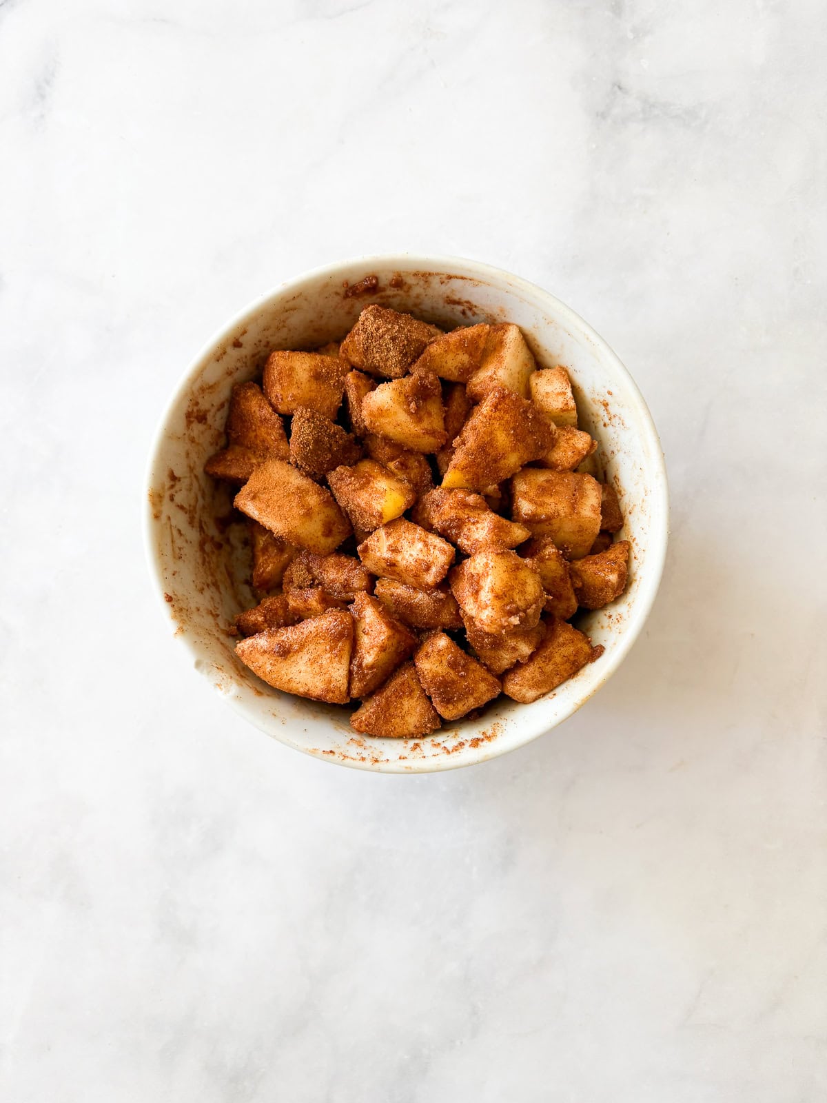 A sweet and simple gluten free apple cake that showcases a tender cake layered with cinnamon-y apples. One-bowl recipe! Apple pieces mixed with sugar and cinnamon in a bowl.