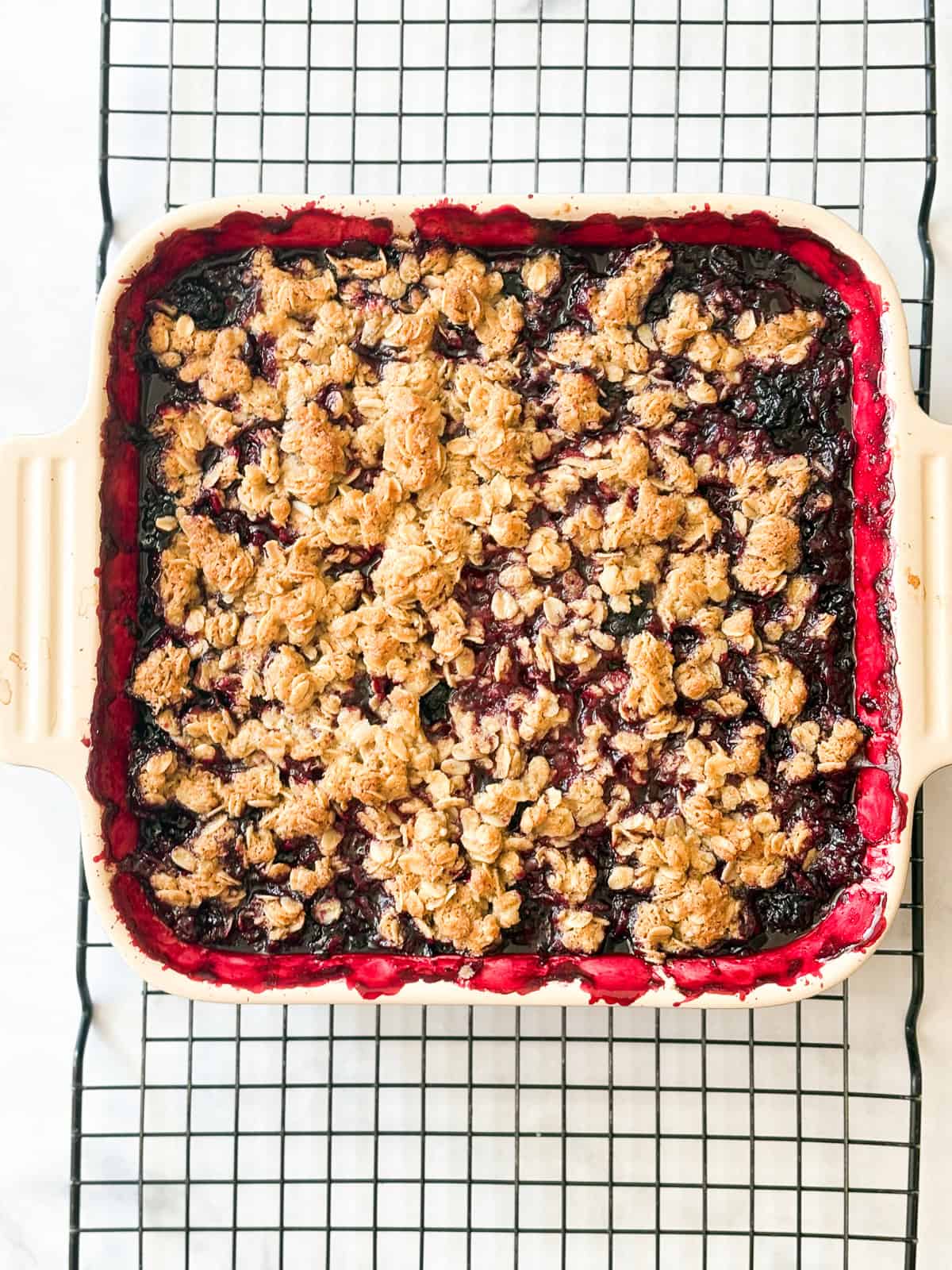 A buttery oat topping floats above a thick, jammy layer of fresh blackberries in this gluten free blackberry crisp. Perfect with ice cream. A pan of gluten free blackberry crisp cools on a rack.