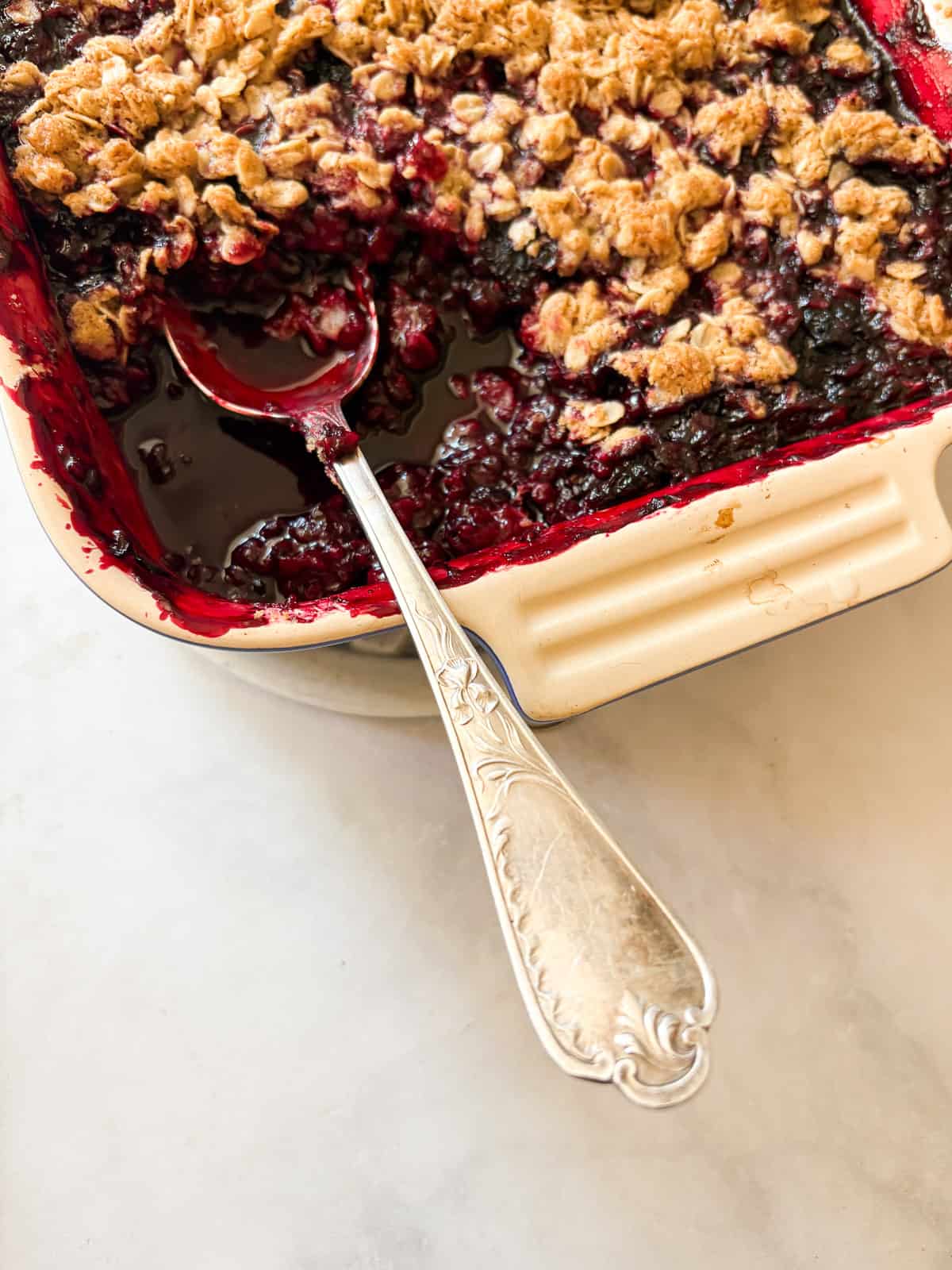 A buttery oat topping floats above a thick, jammy layer of fresh blackberries in this gluten free blackberry crisp. Perfect with ice cream. A pan of gluten free blackberry crisp with a serving spoon.