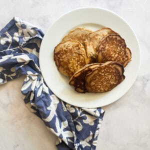 A pile of gluten free buttermilk pancakes on a plate with a blue and white napkin alongside.