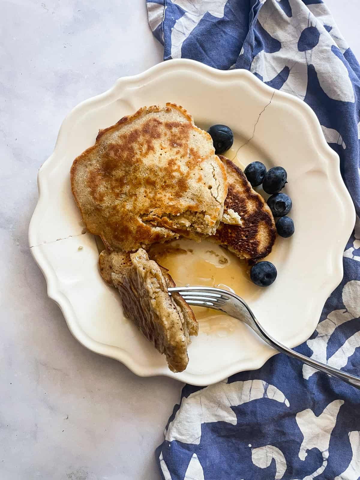 A fork cuts into a maple syrup drenched stack of gluten free buttermilk pancakes.