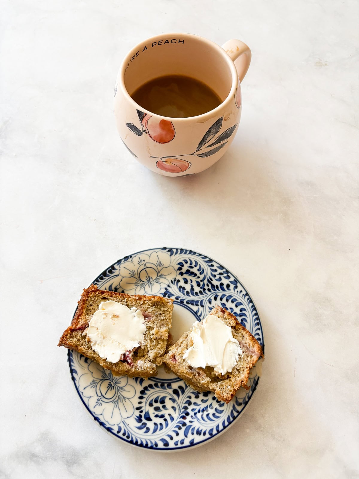 This one-bowl, gluten free easy banana strawberry bread comes together in minutes, and features plenty of chopped fresh strawberries and a kick of cinnamon. A cup of coffee and a piece of banana strawberry bread on a plate.