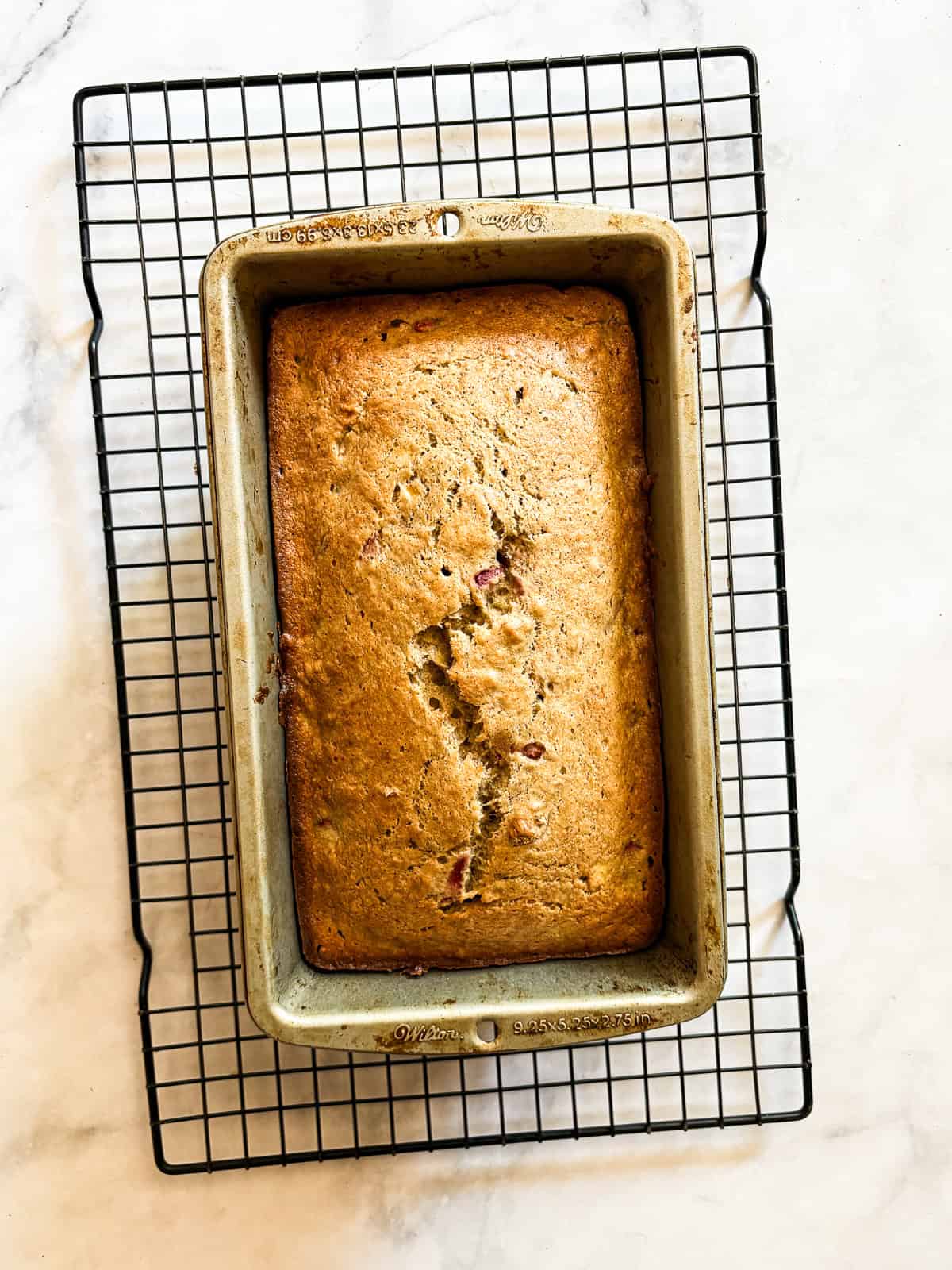 This one-bowl, gluten free easy banana strawberry bread comes together in minutes, and features plenty of chopped fresh strawberries and a kick of cinnamon. A loaf of easy banana strawberry bread cools in the pan.