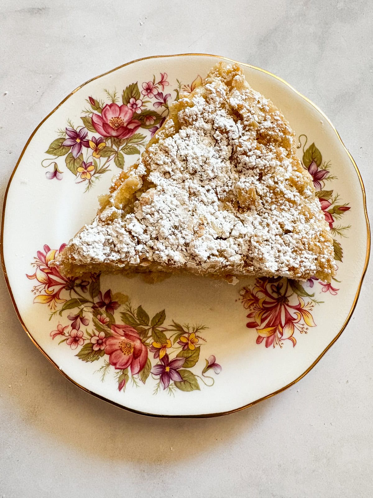 This buttery and tender gluten free French apple cake is inspired by a classic recipe and will almost literally melt in your mouth. A slice of gluten free french apple cake on a plate.
