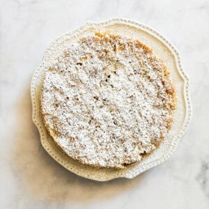 A gluten free french apple cake dusted with powdered sugar on a white plate.