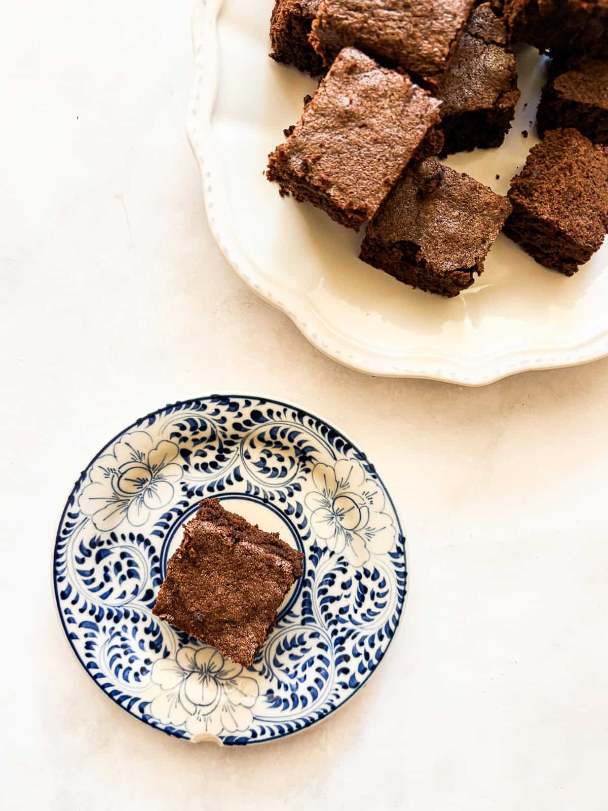 Effortless and gluten-free one bowl brownies are made in, yep, just one bowl. Just mix, pour, and bake to brownie perfection. A homemade brownie on a blue and white plate next to a plate of brownies.