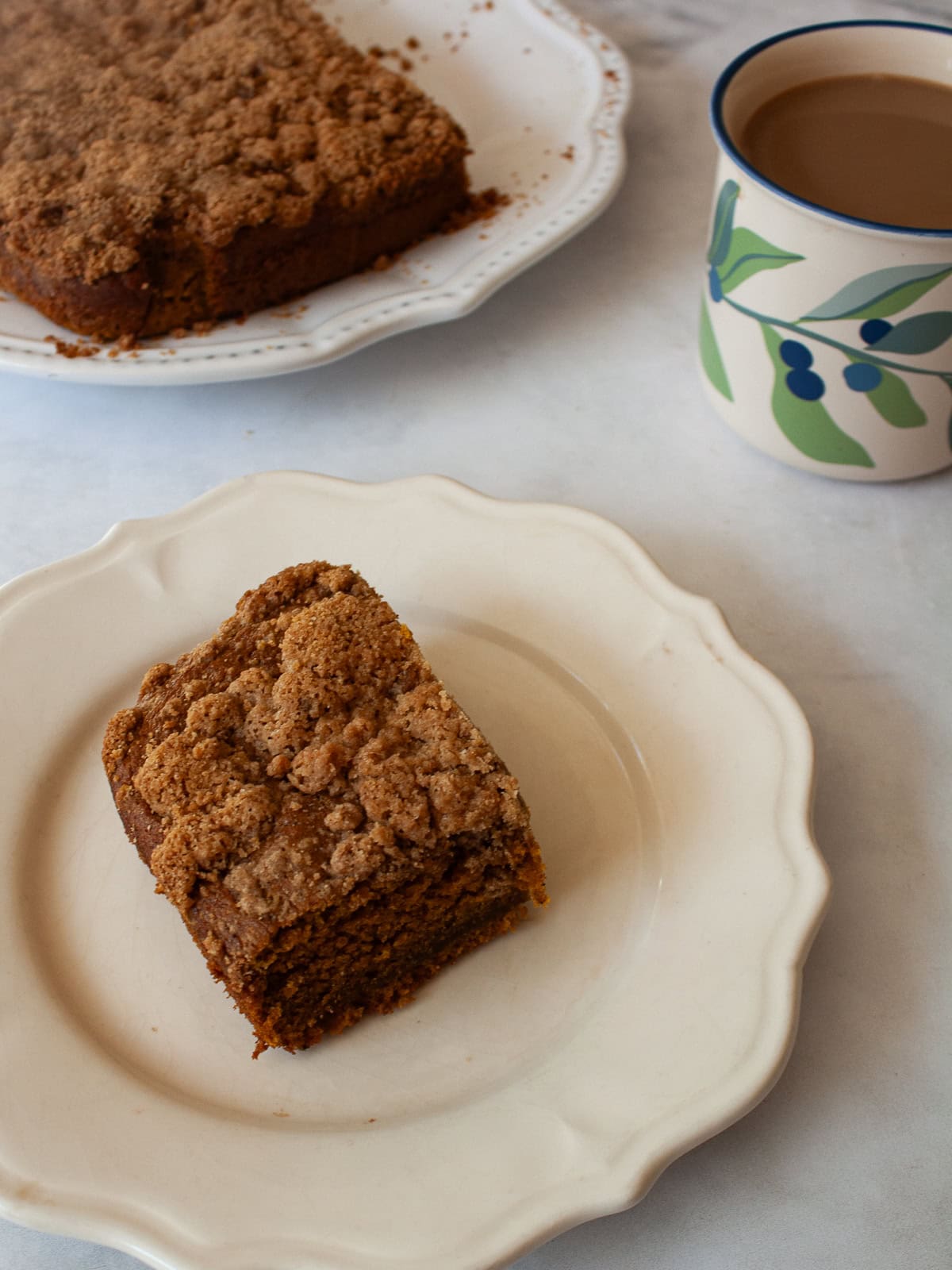 The perfect fall treat, this sweetly spiced and tender gluten free pumpkin coffee cake is topped with a delicious brown sugar streusel. A piece of gluten free pumpkin coffee cake on a plate next to the cake and a cup of coffee.
