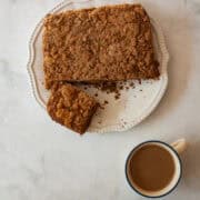 Gluten free pumpkin coffee cake with a piece cut out on a plate with a cup of coffee next to it.