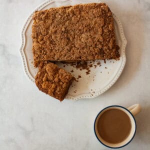 Gluten free pumpkin coffee cake with a piece cut out on a plate with a cup of coffee next to it.