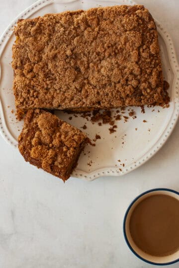 Gluten free pumpkin coffee cake with a piece cut out on a plate with a cup of coffee next to it.