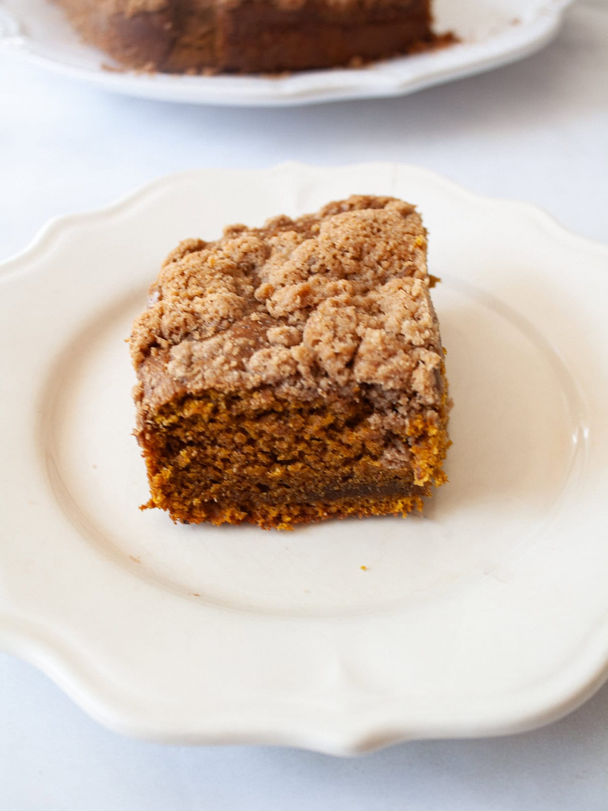 The perfect fall treat, this sweetly spiced and tender gluten free pumpkin coffee cake is topped with a delicious brown sugar streusel. A piece of gluten free pumpkin coffee cake on a white plate.