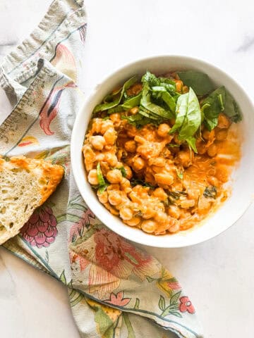 A bowl of marry me chickpeas with bread and a napkin.