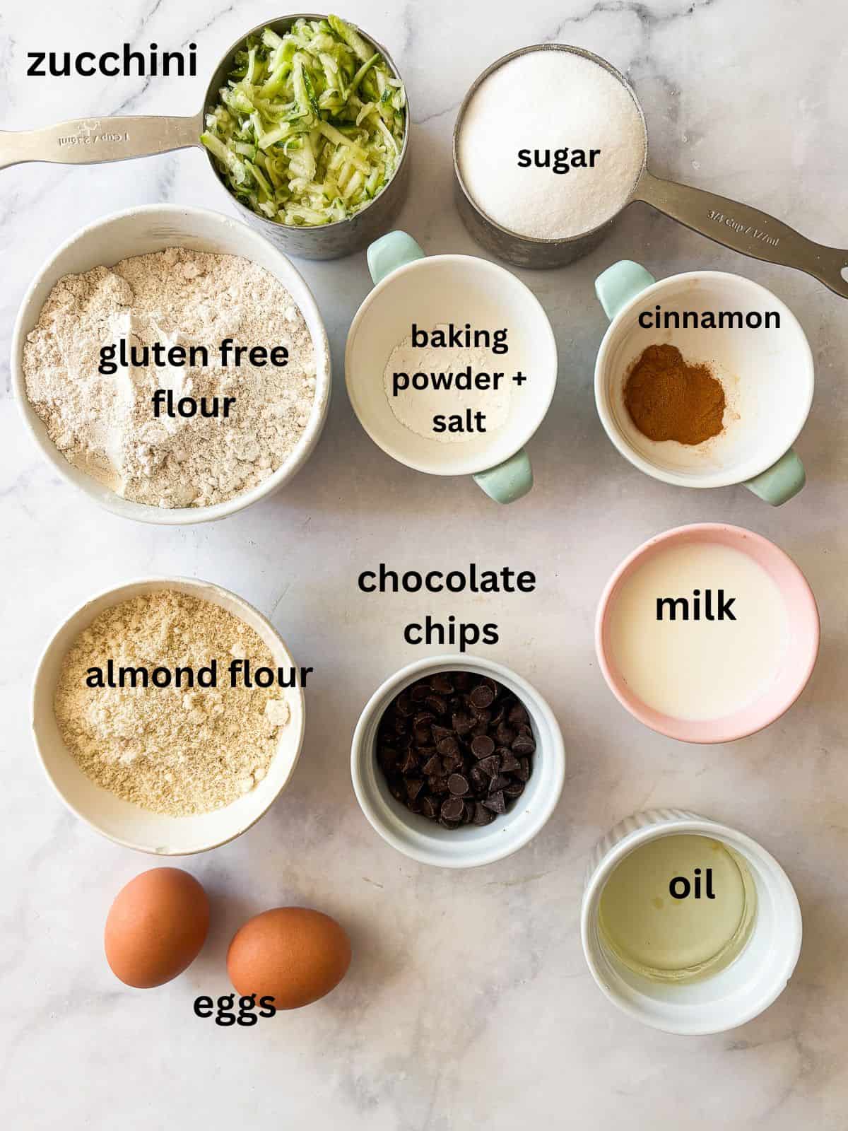 Tuck shredded squash into these gluten free zucchini chocolate chip muffins for a delectable morning treat. Ingredients for gluten free zucchini chocolate chip muffins are text-labeled.