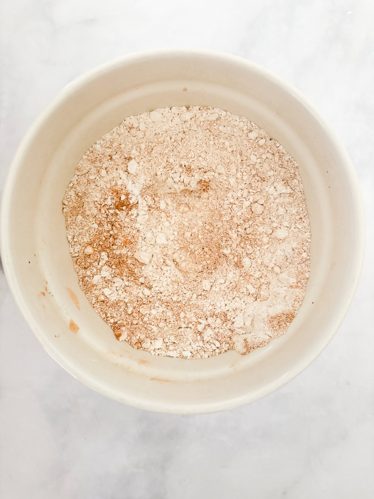 Darkly sweet and studded with walnuts, a gluten free applesauce cake equals homey comfort. Make it with homemade applesauce if you can. Flour mixed with spices in a bowl for gluten free applesauce cake.