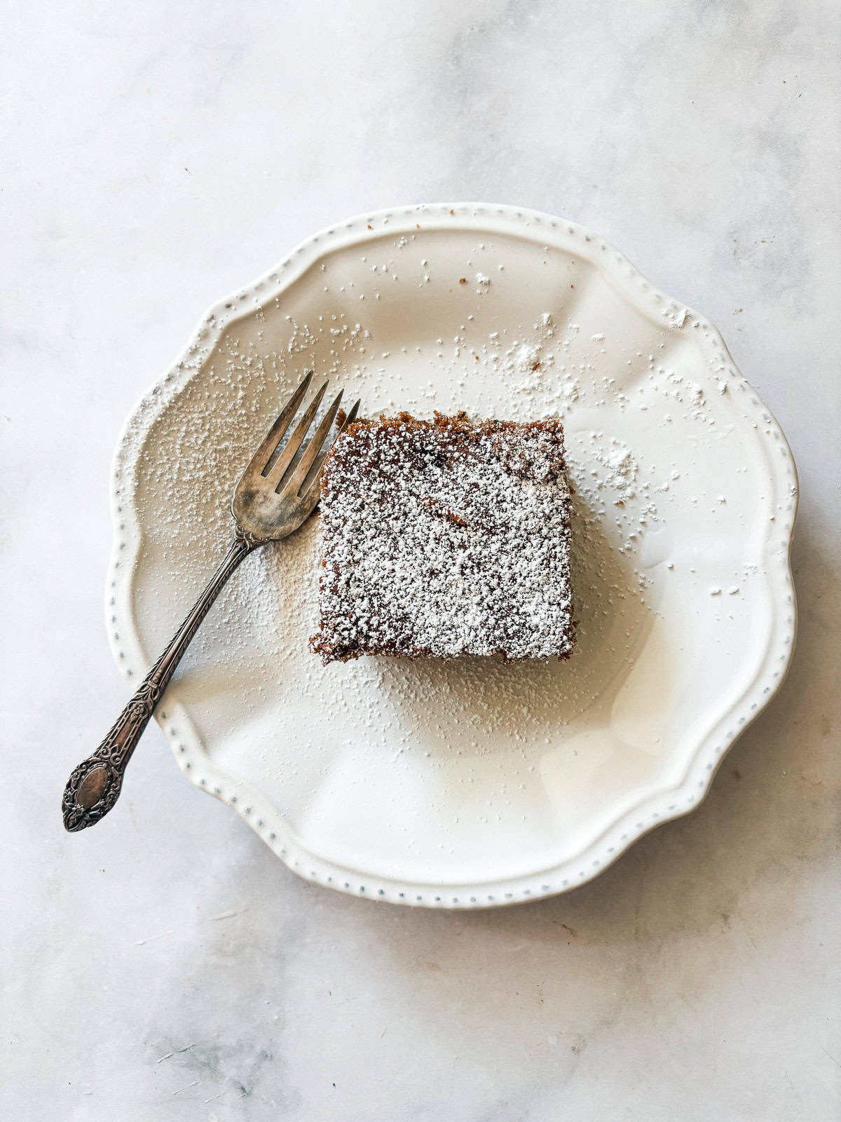 Darkly sweet and studded with walnuts, a gluten free applesauce cake equals homey comfort. Make it with homemade applesauce if you can. A square of gluten free applesauce cake on a plate with a fork.