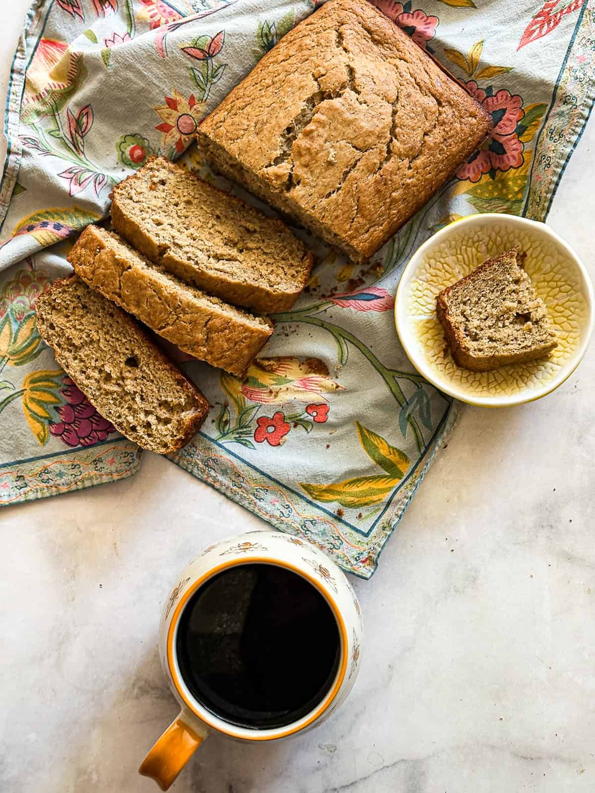 A cup of black coffee next to a loaf of gluten free banana bread.