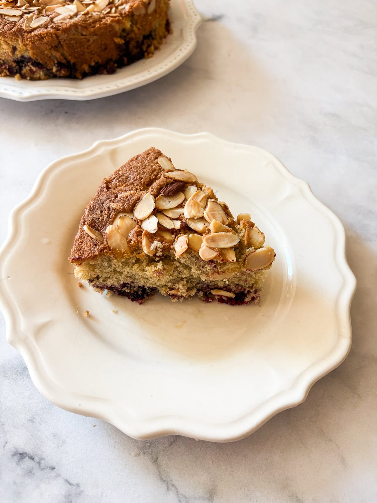 This gluten free blackberry cake features a plush vanilla cake swirled with juicy berries! Delicious and beautiful. A slice of gluten free blackberry cake on a plate.