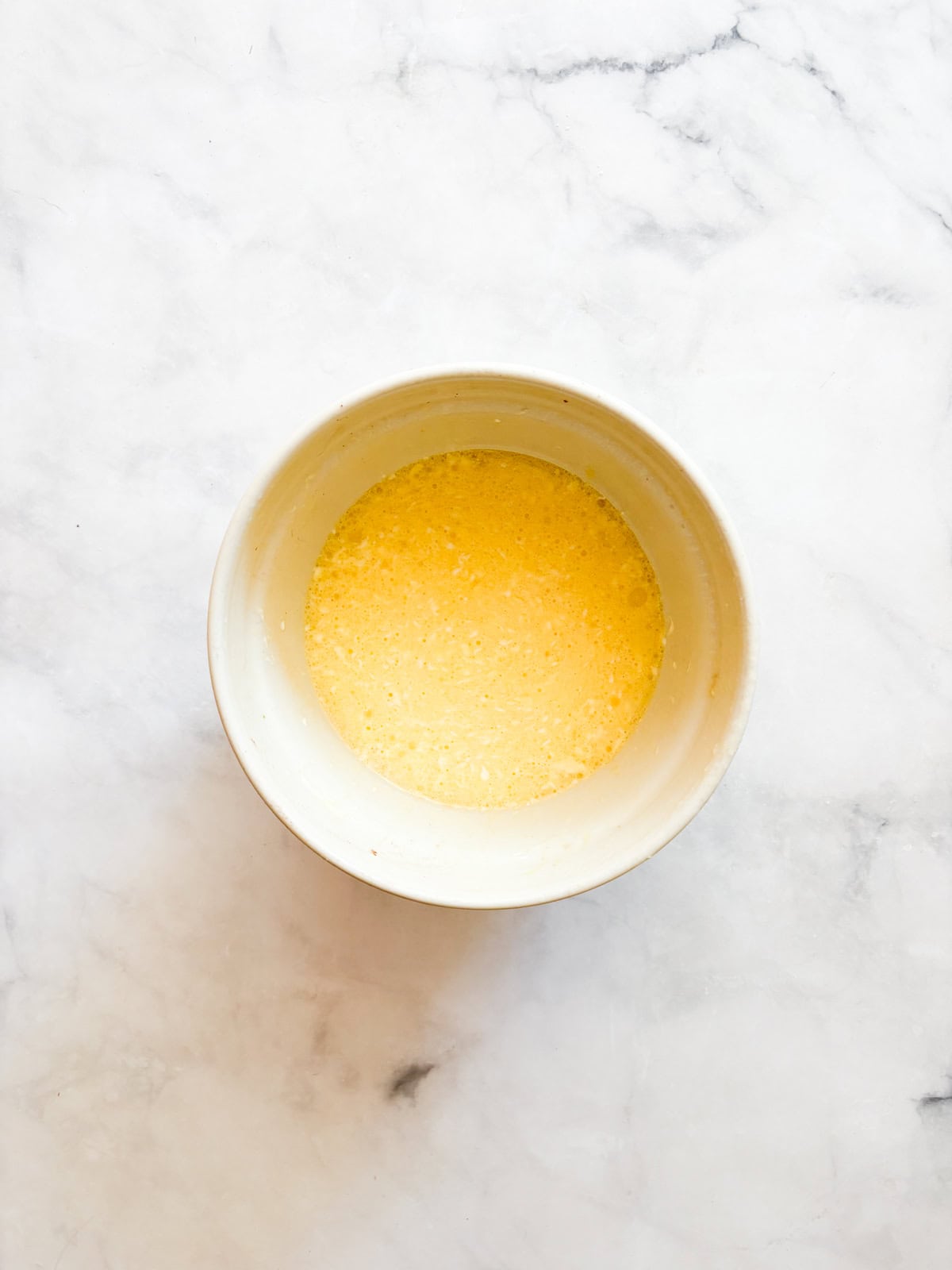 This gluten-free chocolate cake is a deeply dark chocolate cake with a soft and tender crumb that's perfect with fluffy chocolate buttercream. Eggs mixed with oil and buttermilk in a bowl.