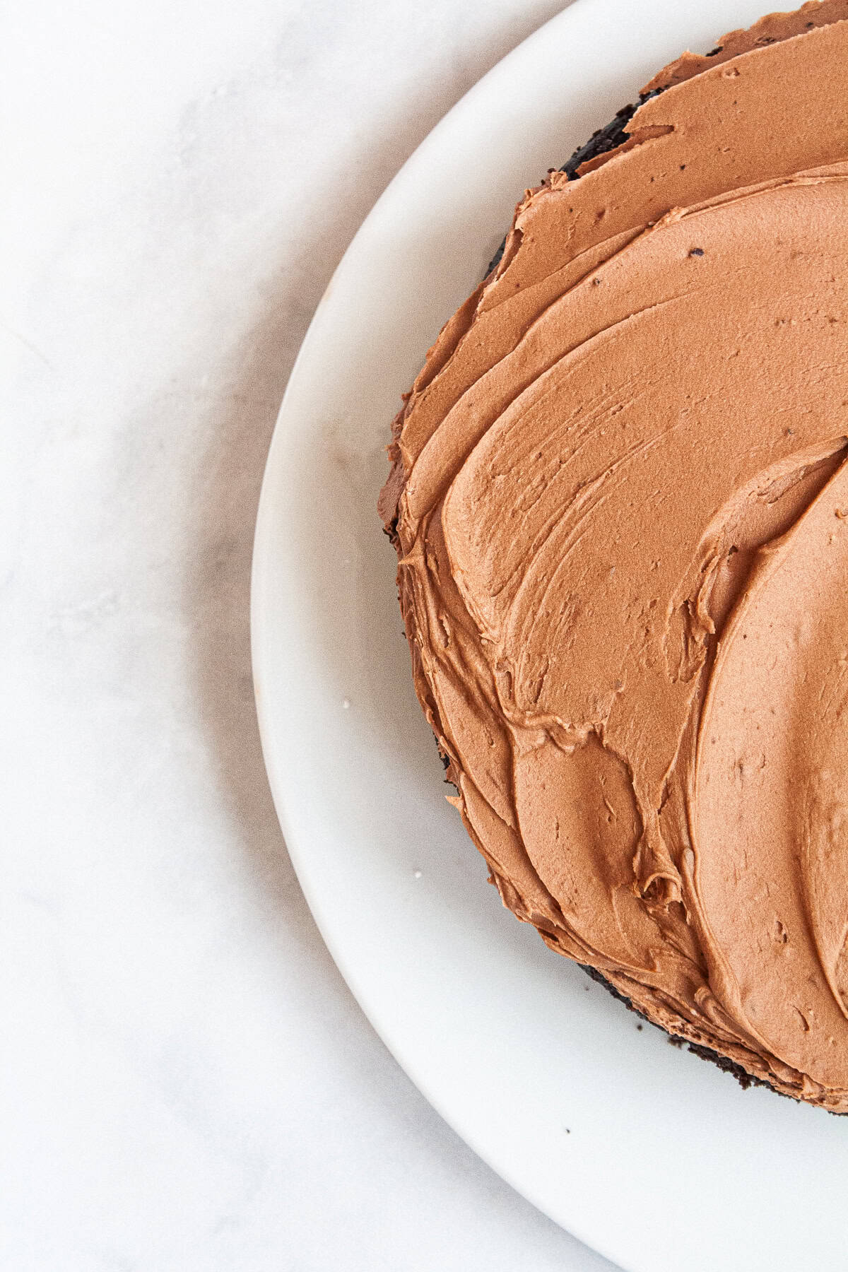 This gluten-free chocolate cake is a deeply dark chocolate cake with a soft and tender crumb that's perfect with fluffy chocolate buttercream. Swirls of chocolate buttercream on top of a gluten-free chocolate cake.